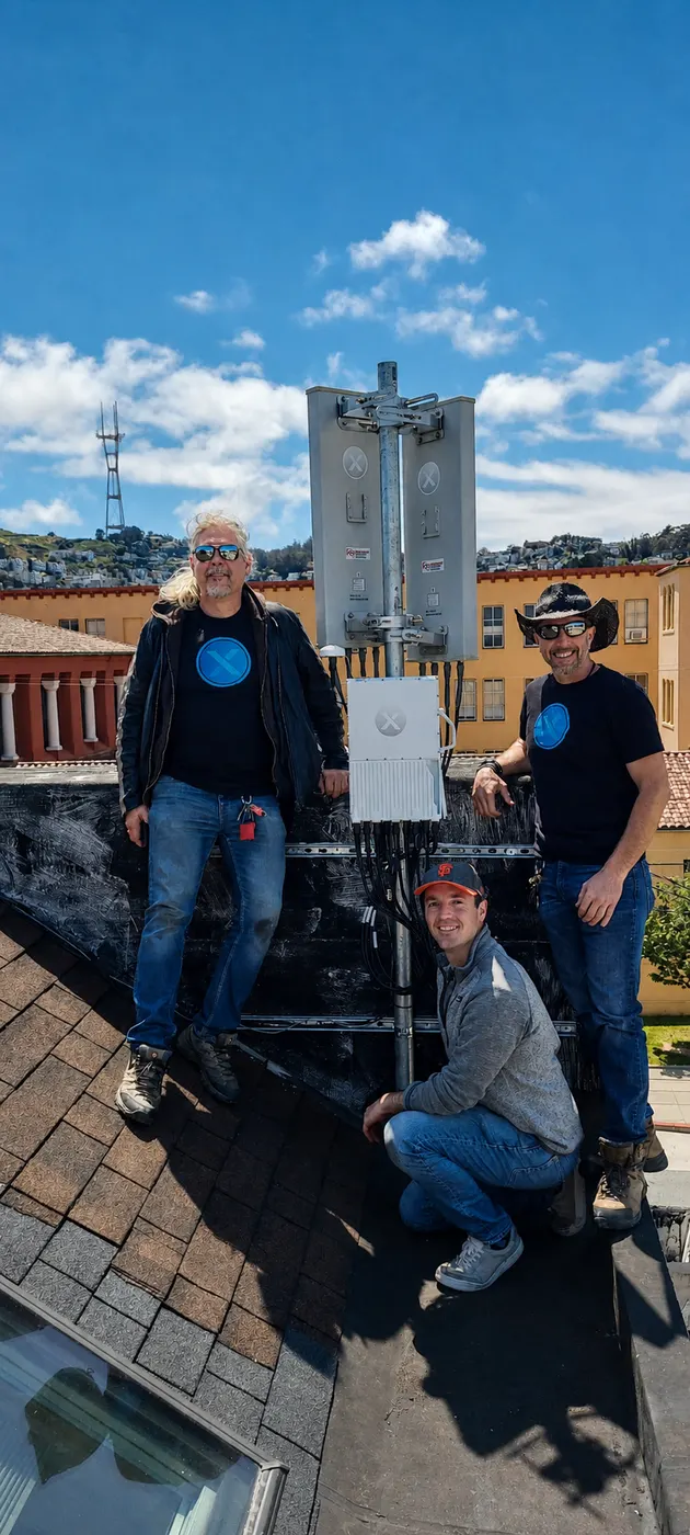 Engineers standing with wireless telecom hardware on a rooftop.