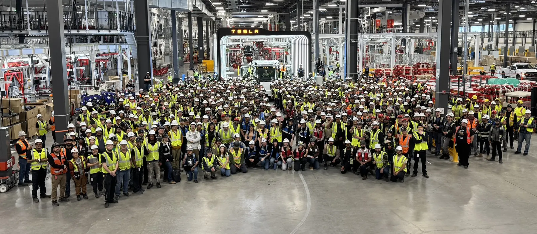 Large Tesla factory team gathered around battery manufacturing equipment.